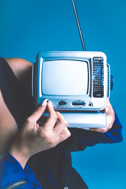 A woman holds a retro portable TV against a vibrant blue background, evoking nostalgia.