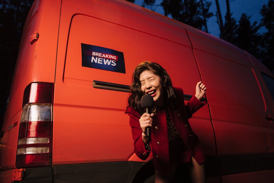 Asian woman reporter energetically broadcasting with a microphone in front of a news van at night.